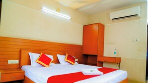 Une chambre d’hôtel avec un lit en bois, du linge de lit blanc, des oreillers rouges, un plaid rouge, une table de chevet, une armoire en bois et un appareil de climatisation.