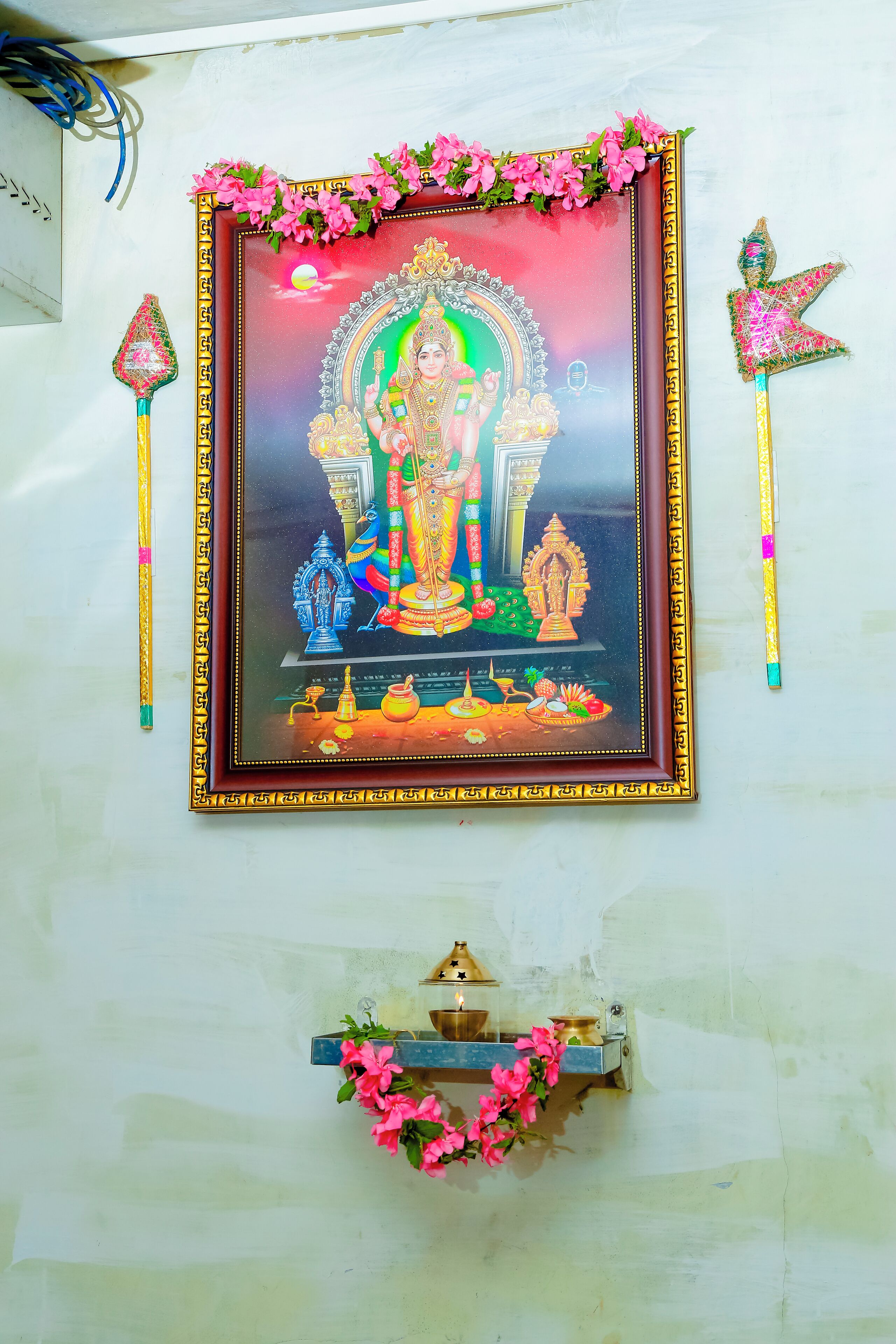 A framed religious painting with a decorative border, a small shrine below, and two ceremonial items on either side.