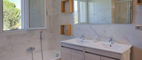 A modern bathroom with a bathtub, two sinks, and a large mirror.