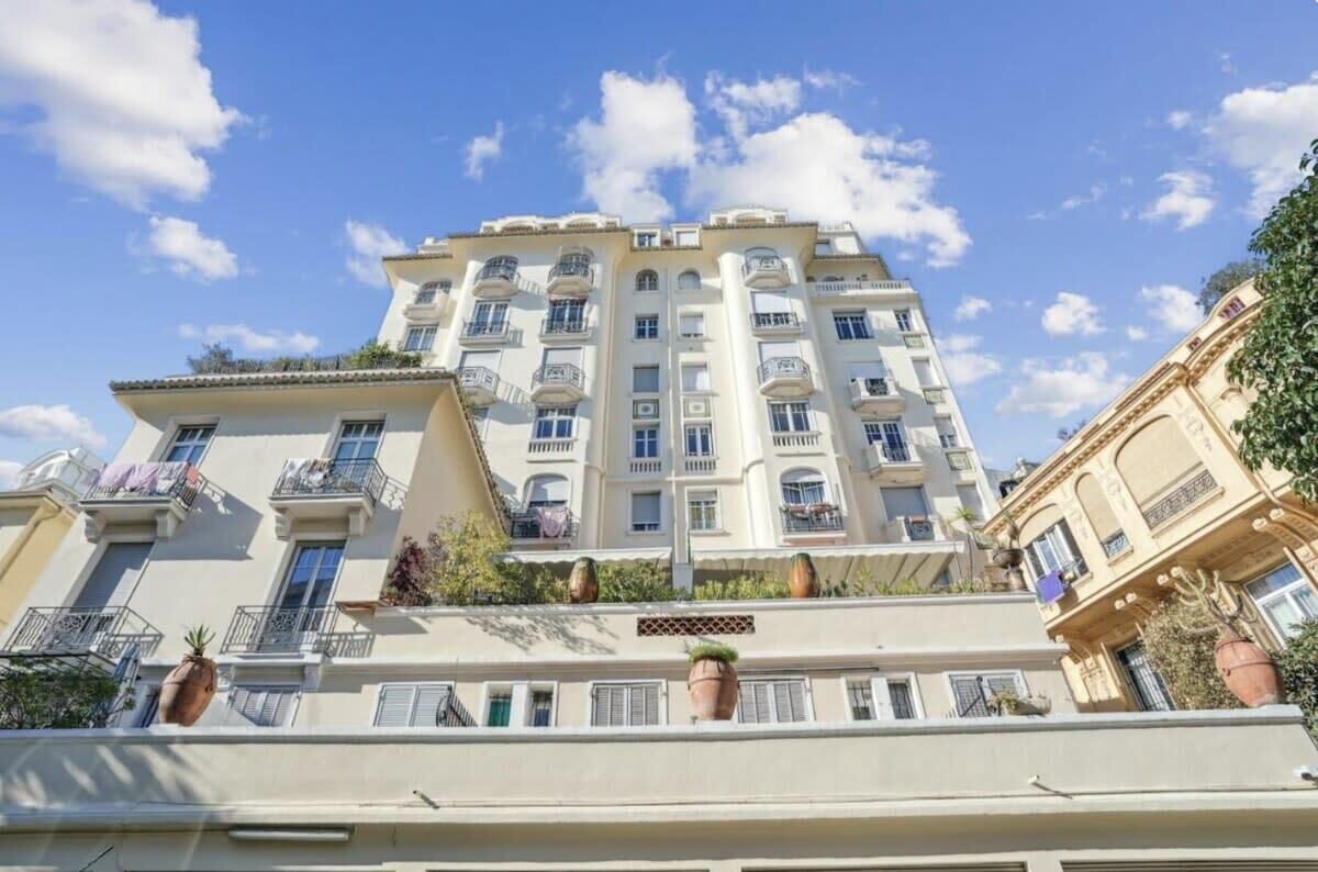 A multi-story residential building with balconies, a flat roof, and a clear blue sky.