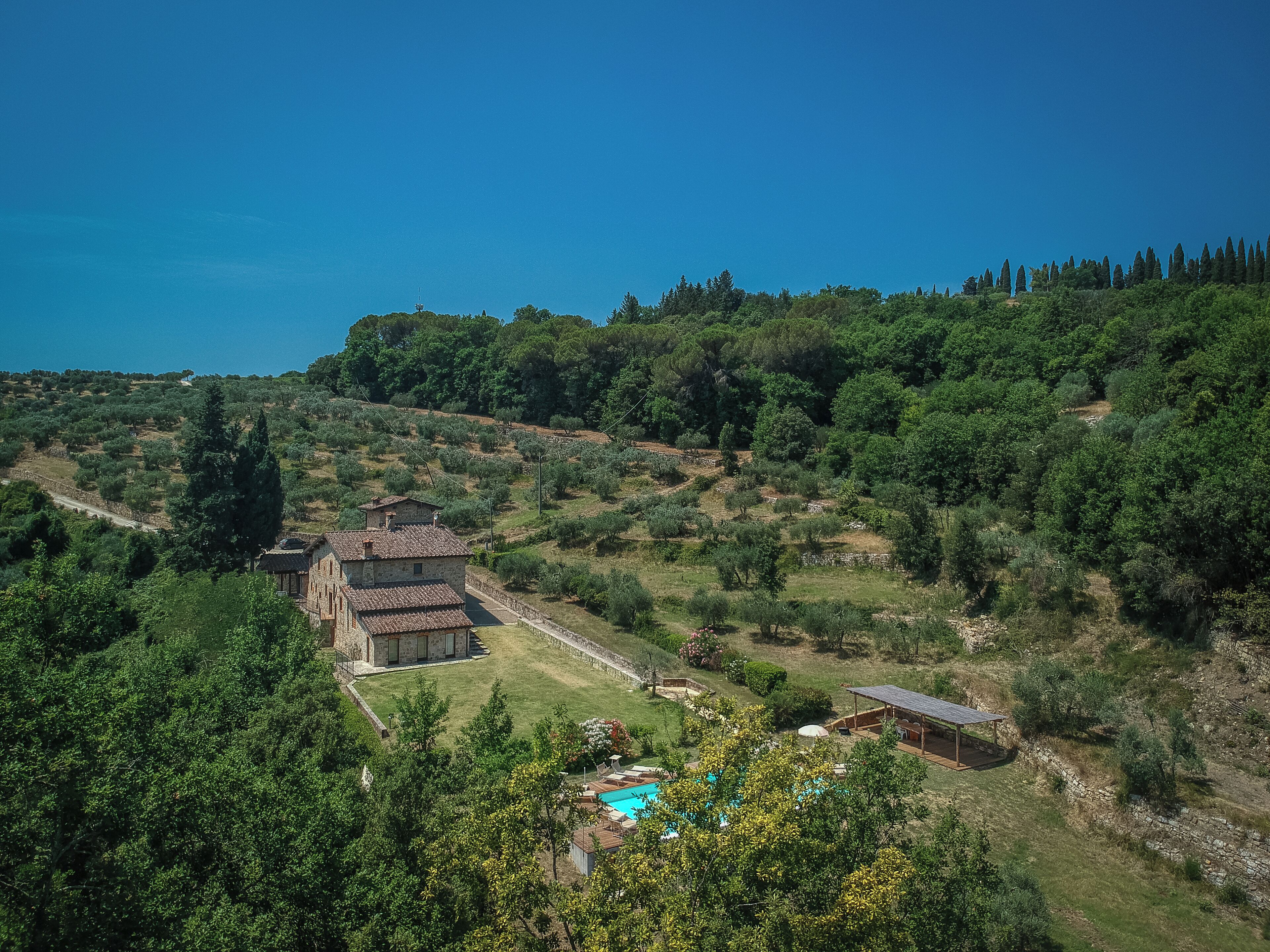 A rustic stone house with a tiled roof, a swimming pool, and a garden.