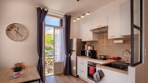 A compact kitchen with a large window, a clock, and a small dining table. - Villa Sandrine (Calvi)