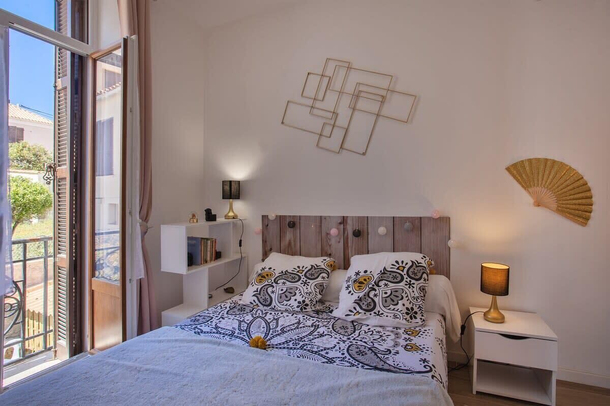 A bedroom with a bed, bedside tables, a wall-mounted fan, and a window with curtains.
