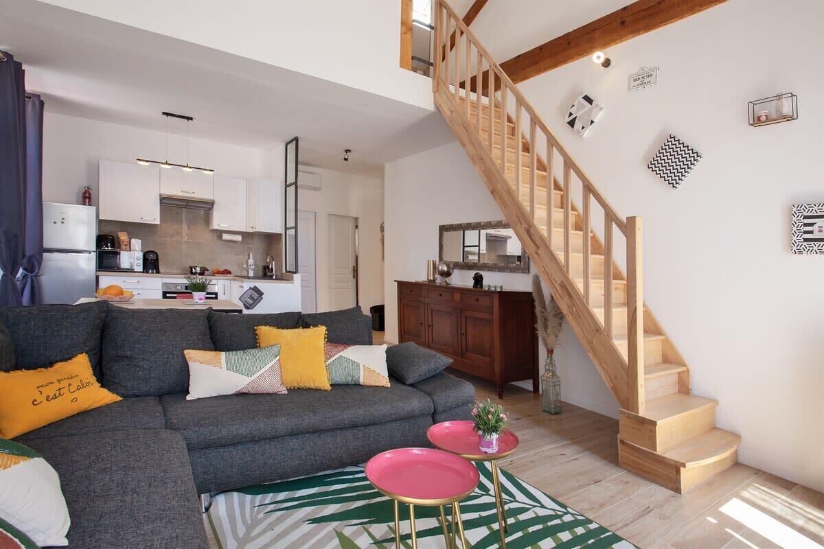 A modern living room with a grey sofa, a staircase, and a kitchen in the background.