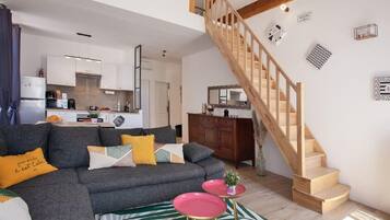 A modern living room with a grey sofa, a staircase, and a kitchen in the background.