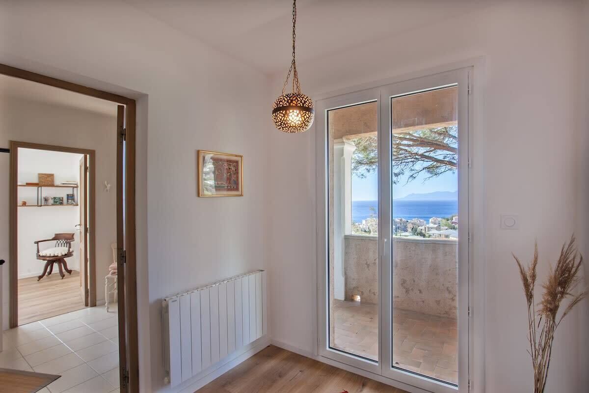 A room with a large sliding glass door leading to a balcony with a view of the sea.