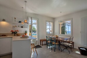Una cocina luminosa con armarios blancos, una mesa de comedor con sillas y ventanas grandes que ofrecen vistas al exterior.
