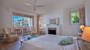 Quarto com uma cama grande, lareira, ventilador de teto e varanda com cadeiras.