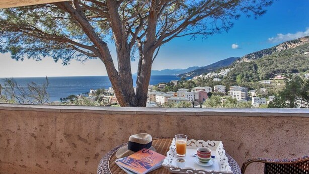 Uma varanda com uma mesa de vime, um chapéu, uma revista e uma bandeja com um copo de suco de laranja e uma chávena.