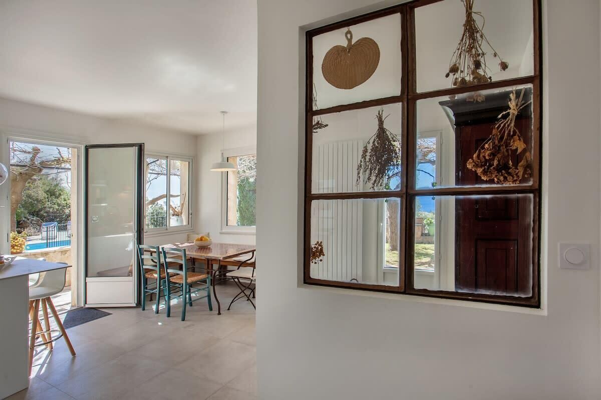 A dining area with a table and chairs, a view through a window, and a door leading outside.