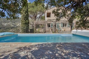 Una piscina con solárium de piedra, rodeada de árboles y un edificio con balcón.