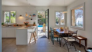 Uma cozinha moderna com uma ilha central, uma área de jantar com mesa e cadeiras de madeira, e grandes janelas que proporcionam luz natural.