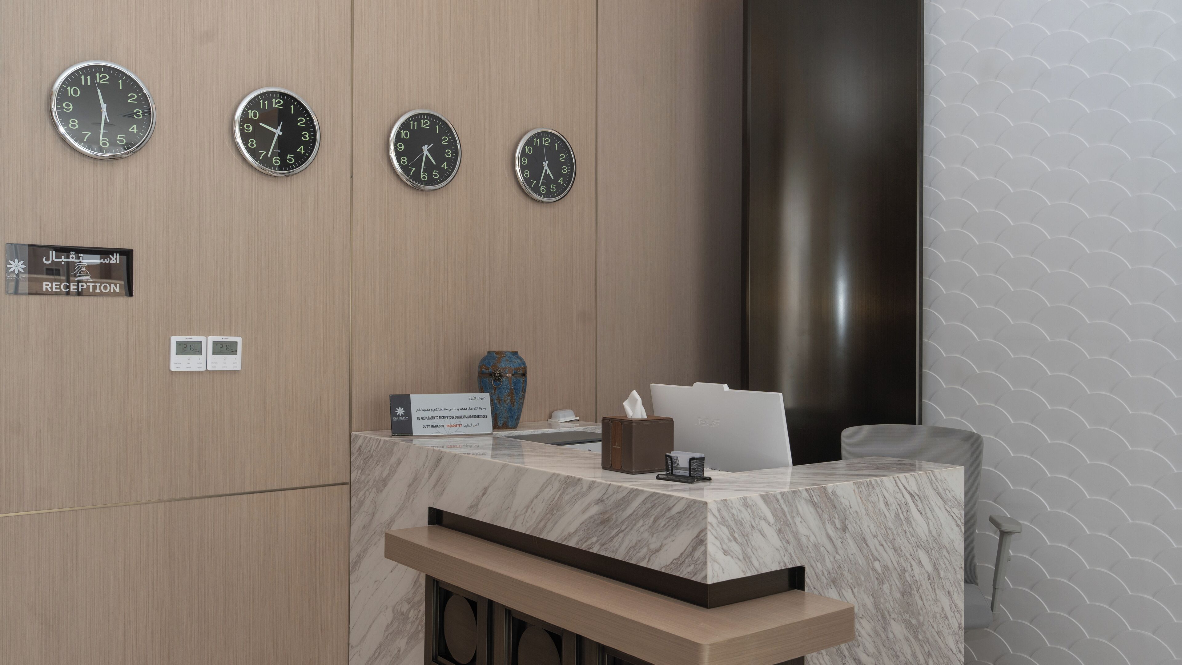 A reception desk with three clocks, a reception sign, a digital display, a vase, and a tissue box.