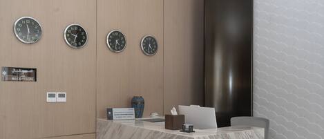 A reception desk with three clocks, a reception sign, a digital display, a vase, and a tissue box.