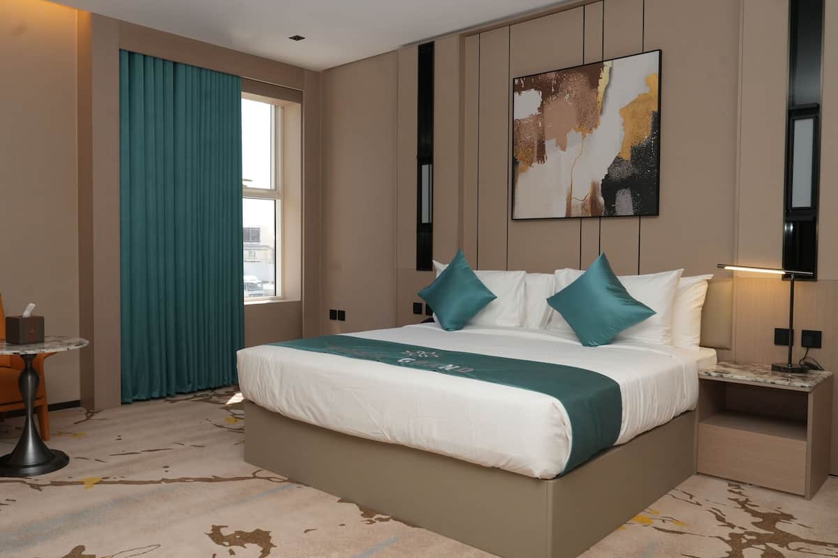 A hotel room with a bed, a chair, a small table, a lamp, and a painting on the wall.
