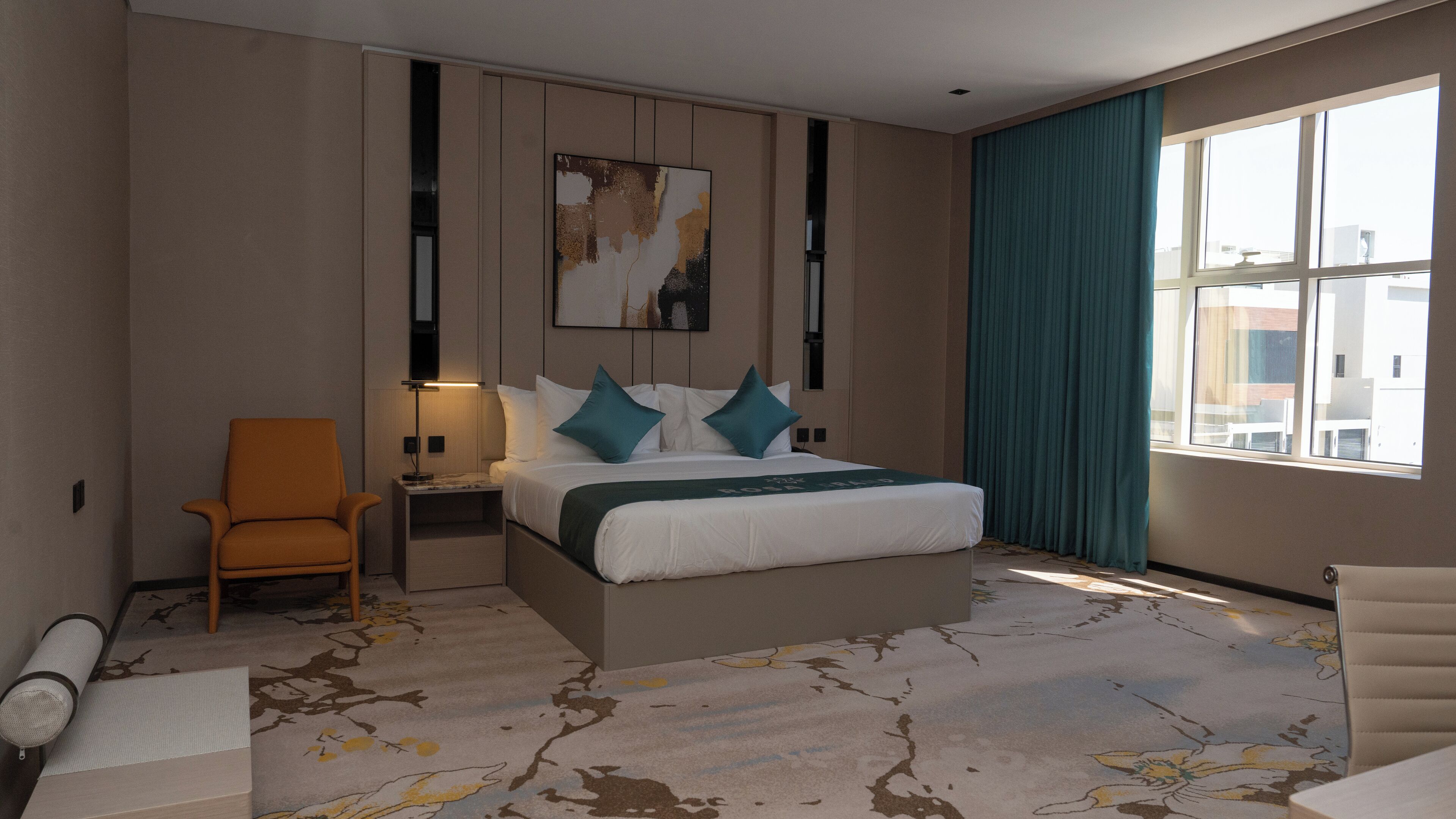 A hotel room with a large bed, a nightstand, a chair, a desk, and a window with curtains.