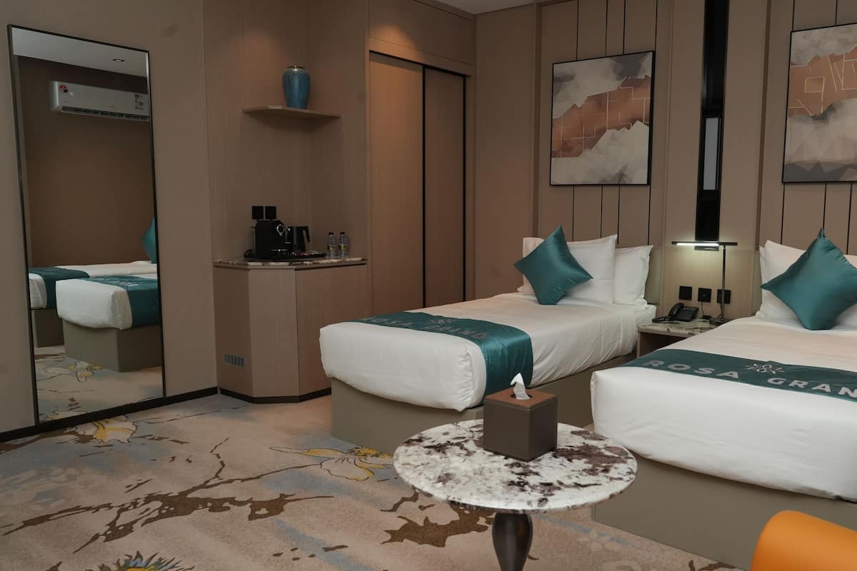 A hotel room with two beds, a small desk, a coffee machine, a mirror, and artwork on the walls.