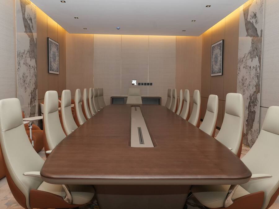 Ein Konferenzraum mit einem langen Tisch, mehreren Stühlen und einer Projektionsleinwand.