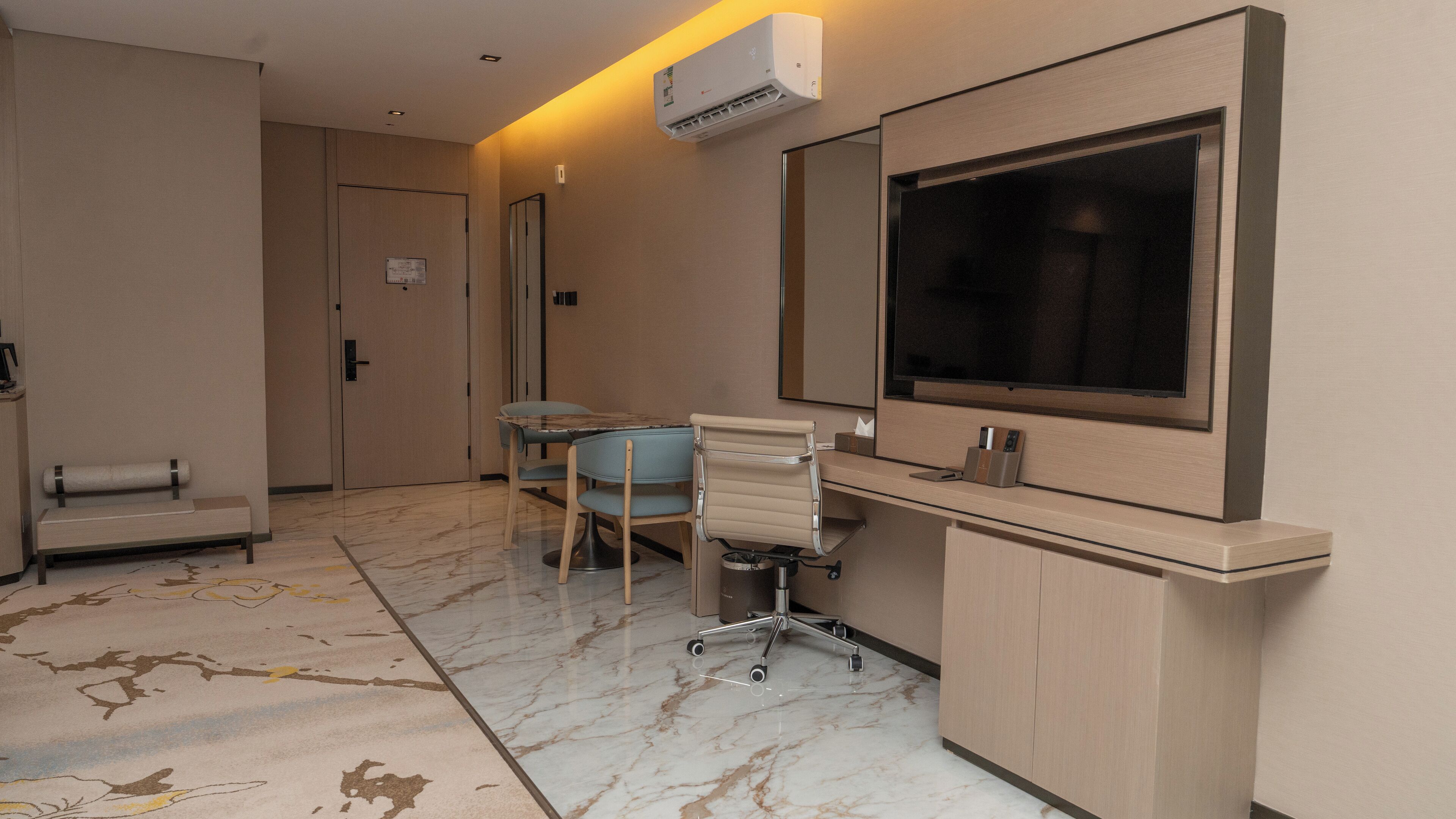 A hotel room with a large mirror, a desk with a chair, a small table, and a sofa.