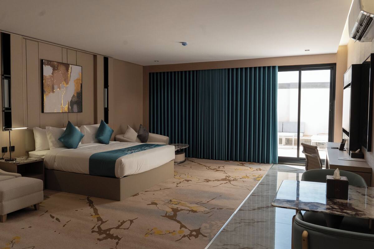 A modern hotel room with a large bed, a desk, a chair, a sofa, and a view of the outdoors.