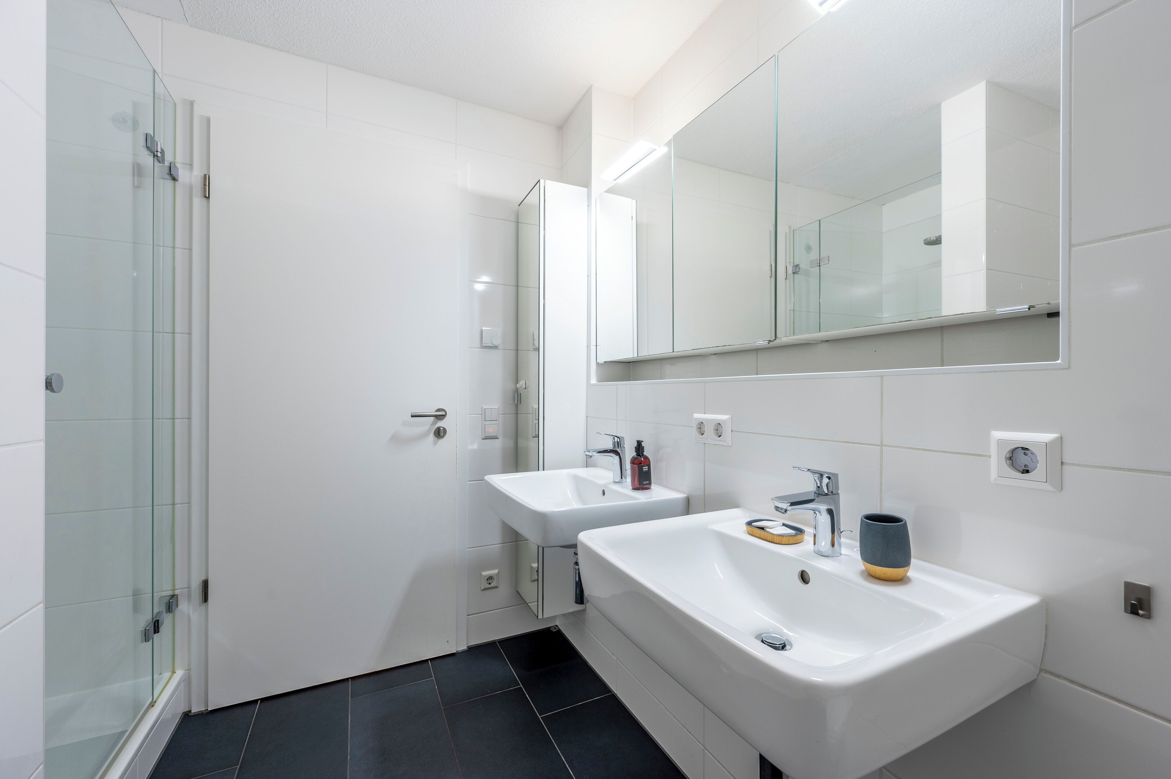 Une salle de bain moderne dotée d’une douche à parois de verre, de deux lavabos et d’un grand miroir.