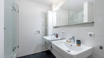 Une salle de bain moderne dotée d’une douche à parois de verre, de deux lavabos et d’un grand miroir.