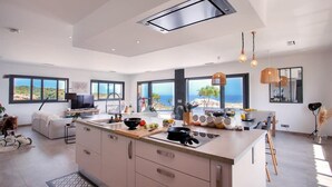 A modern kitchen with a large island, large windows, and a view of the sea.
