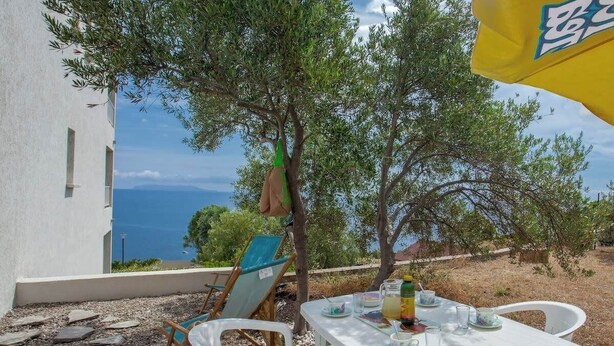 A table set outdoors with a view of the sea, a tree, and a building in the background. - Casa Le Sureau (Pino)