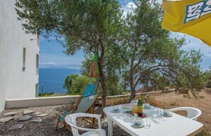 Mesa al aire libre con vista al mar, un árbol y un edificio al fondo.