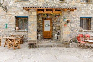 A stone building with a wooden door, outdoor seating, and a sign indicating it is a hostel. - Casa Rural Hostel dos Lucas (OROS BAJO)