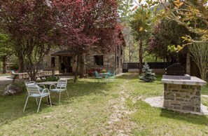A stone building with a porch, surrounded by a grassy yard with metal chairs and a small table. - Casa Rural Hostel dos Lucas (OROS BAJO)