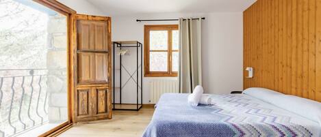 Ein Schlafzimmer mit einem Bett, einem Holzschrank, einem Fenster mit Vorhängen und einem Balkon.