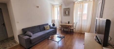 A living room with a sofa, a coffee table, a TV, and a dining area with chairs and a table.