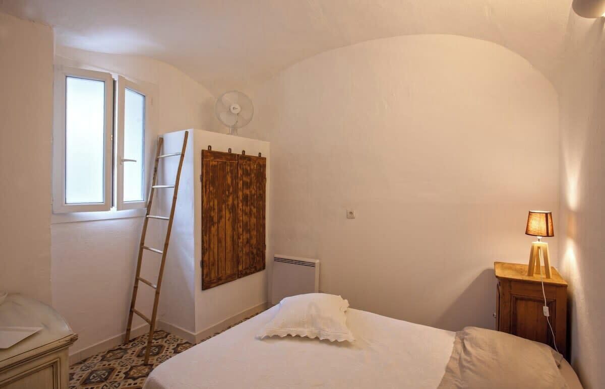 A bedroom with a bed, a ladder, a wardrobe, a window, a radiator, and a bedside lamp.
