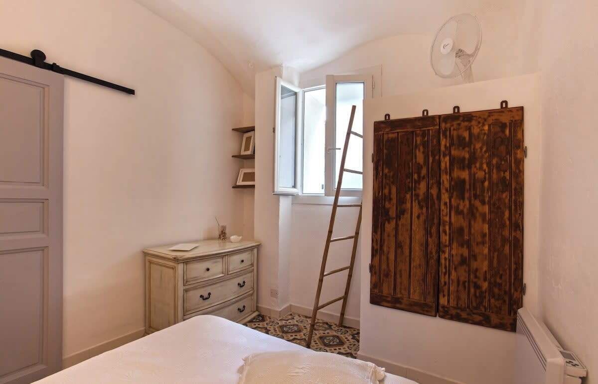 Une chambre à coucher avec un lit, une commode, une armoire, une fenêtre et une échelle.