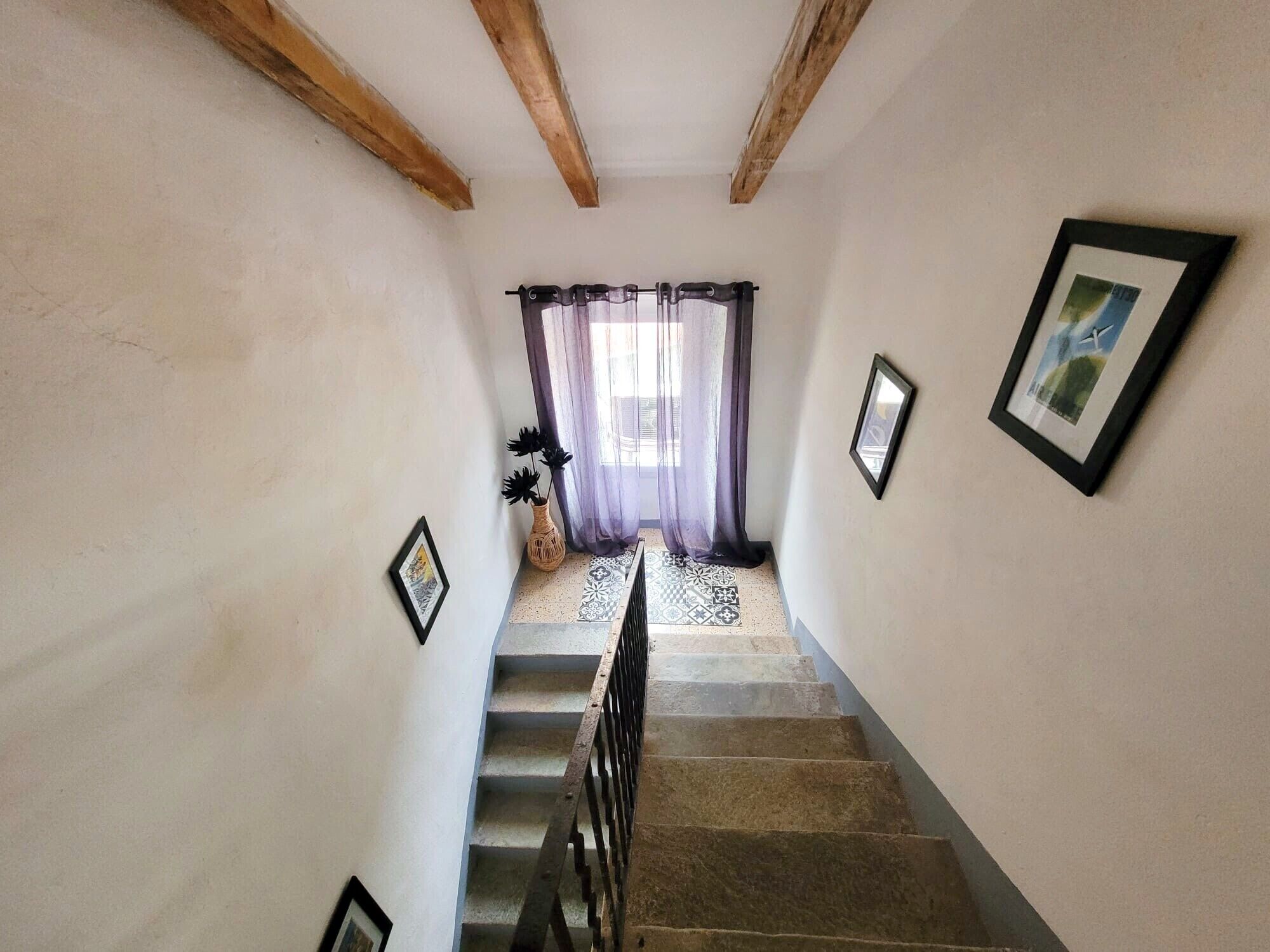 Eine Treppe mit hölzernem Geländer, einem gemusterten Boden und einem Fenster mit durchsichtigen Vorhängen.