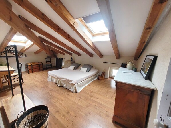 Een slaapkamer met een loft-stijl plafond, houten balken, een bed, een bureau, een stoel, een kledingkast en een raam.