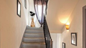 A staircase with a black railing, a wall-mounted light, and framed pictures. - Casa Torra. (Omessa)