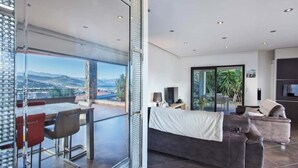 A modern living room with a large window, a sofa, and a dining area with a table and chairs.