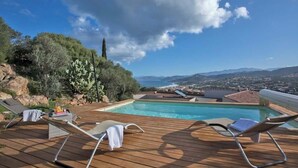 A wooden deck with lounge chairs and a swimming pool overlooking a scenic landscape.