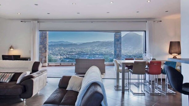 A modern living room with a large window offering a city and mountain view.