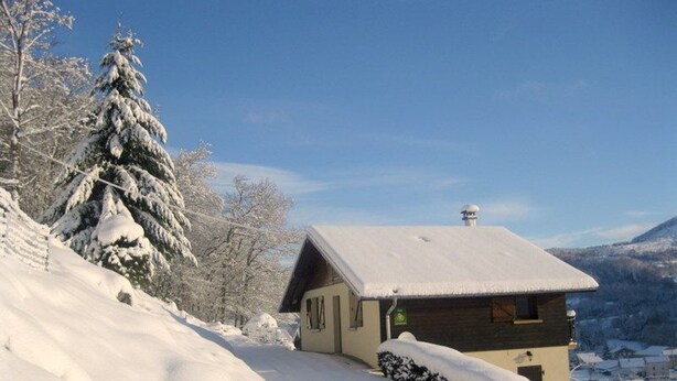 Ein mit Schnee bedecktes Blockhaus mit geneigtem Dach, gelegen an einem verschneiten Berghang mit freiem Blick auf die umliegenden Berge.