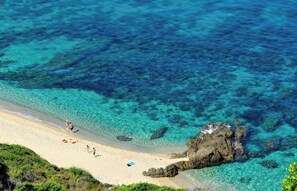 A beach with clear turquoise water, rocky outcrops, and people walking along the shore. - Casa Ortale (Monticello)
