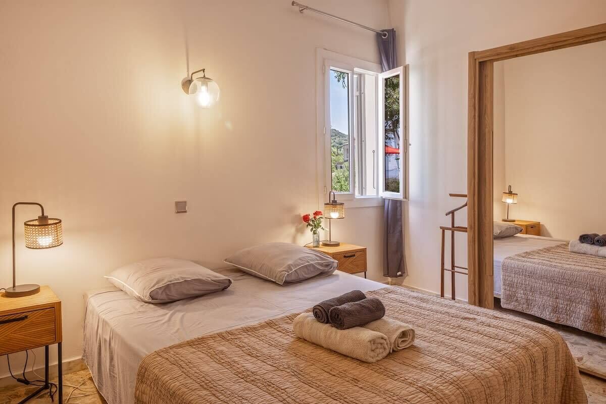 Ein Schlafzimmer mit Bett, Nachttisch, Lampe, Fenster und Spiegel.
