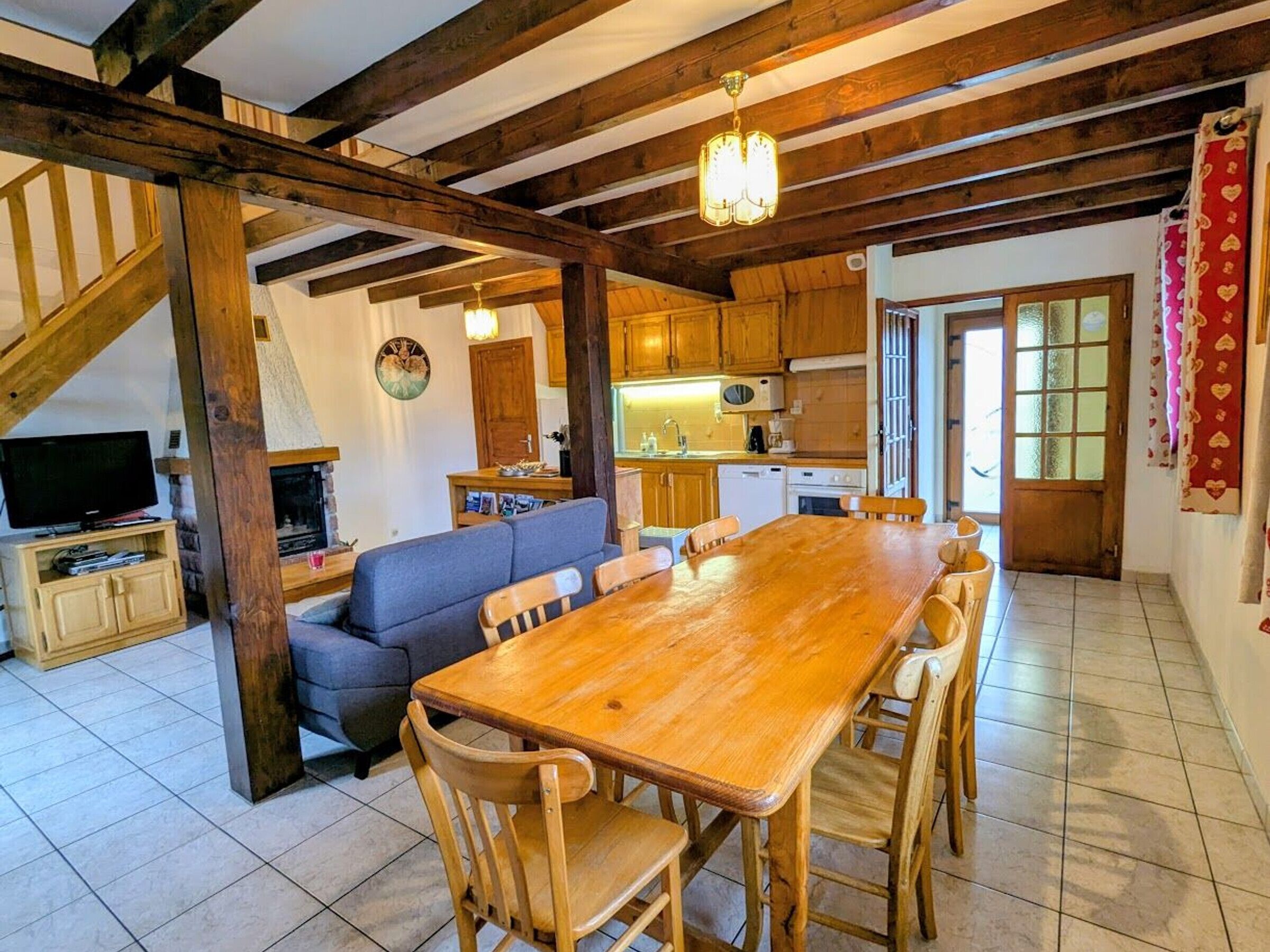 A spacious living area with a wooden dining table, a sofa, and a television.