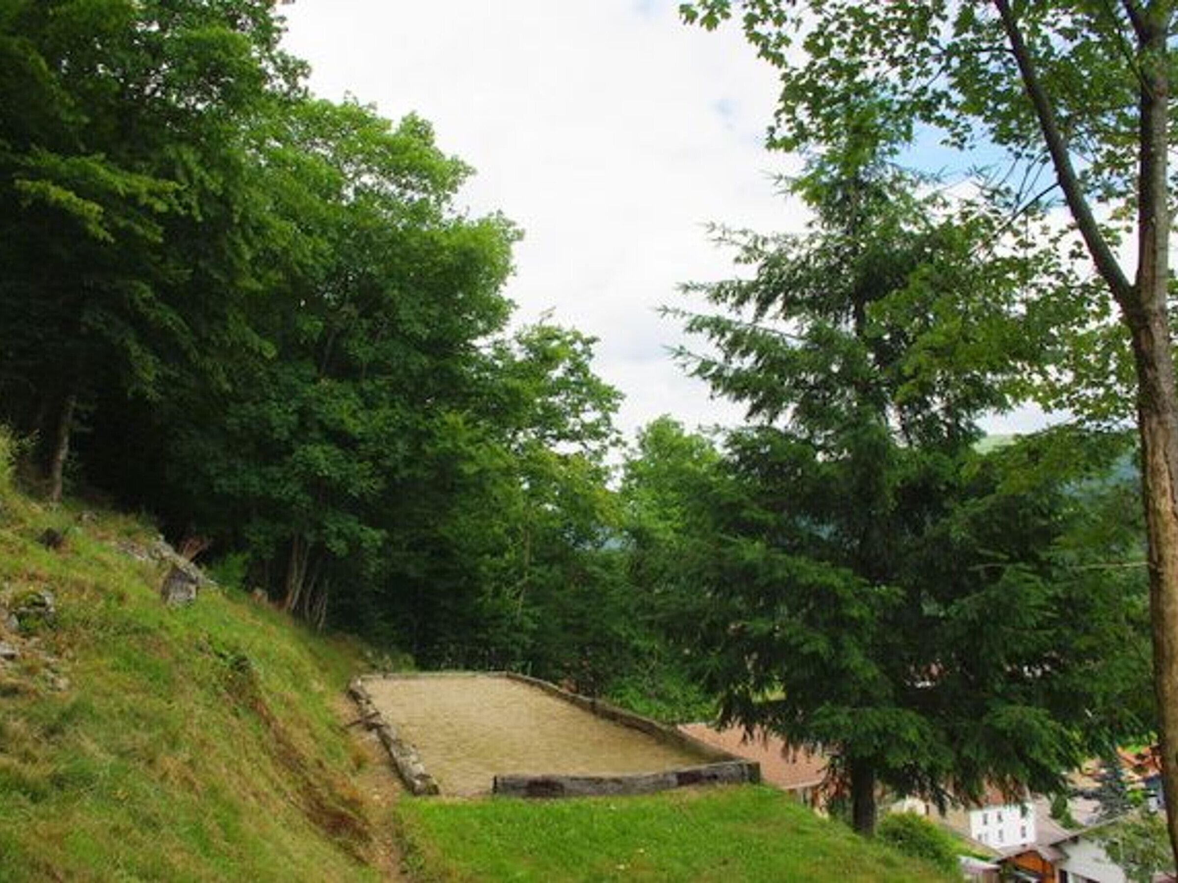 Una zona erbosa con una struttura in pietra, circondata da alberi.