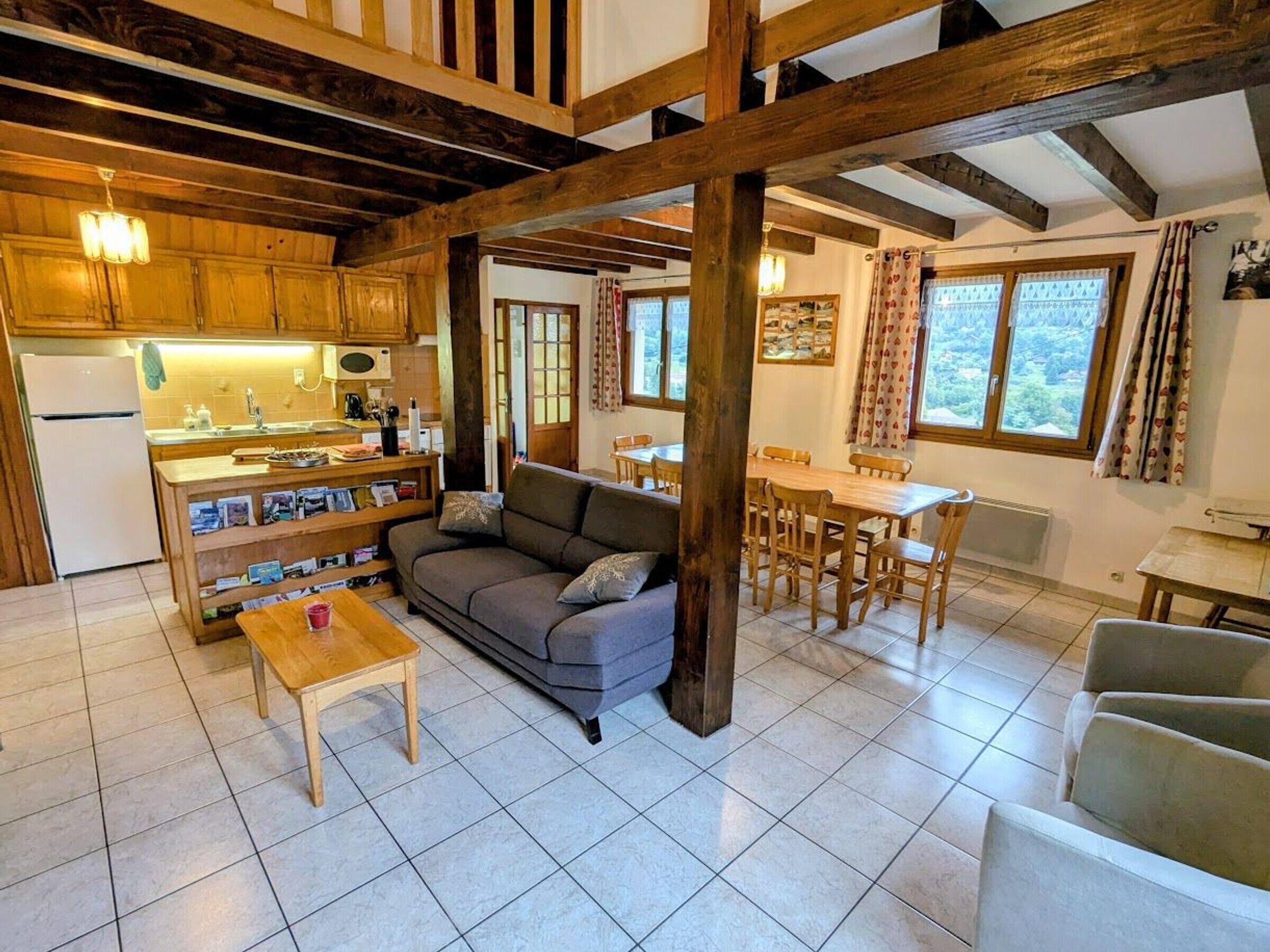 A cozy living room with a sofa, a coffee table, and a dining area with a table and chairs. There is a kitchen with wooden cabinets and a refrigerator.