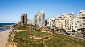 A coastal cityscape with modern high-rise buildings, a beach, and a roundabout with cars. - Netanya Beach & Pool Stay by Sea N' Rent (Netanya)
