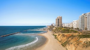 A coastal cityscape with a sandy beach, a rocky breakwater, and high-rise buildings. - Netanya Beach & Pool Stay by Sea N' Rent (Netanya)