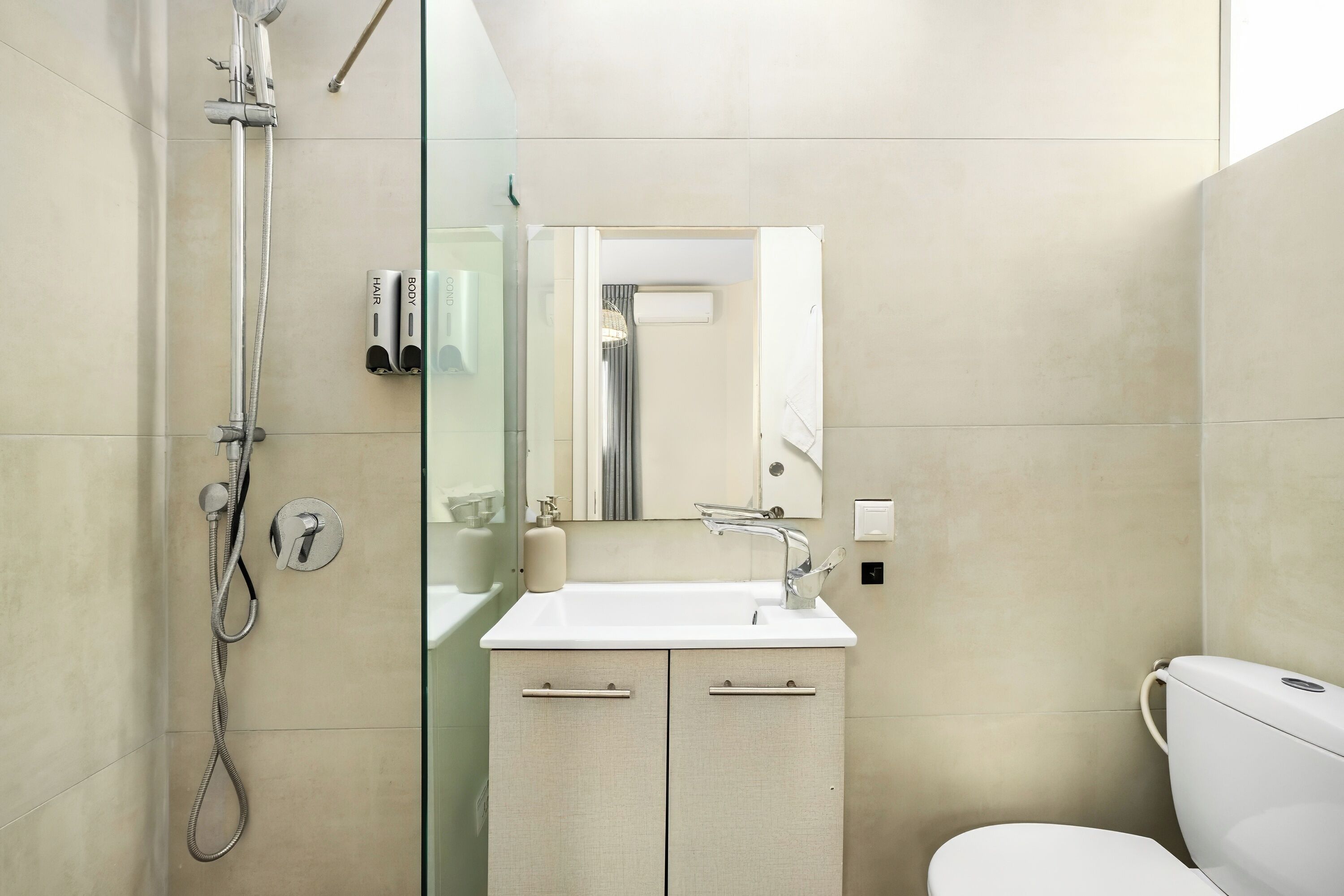 Un baño moderno con ducha de vidrio, un lavabo con espejo y un inodoro.